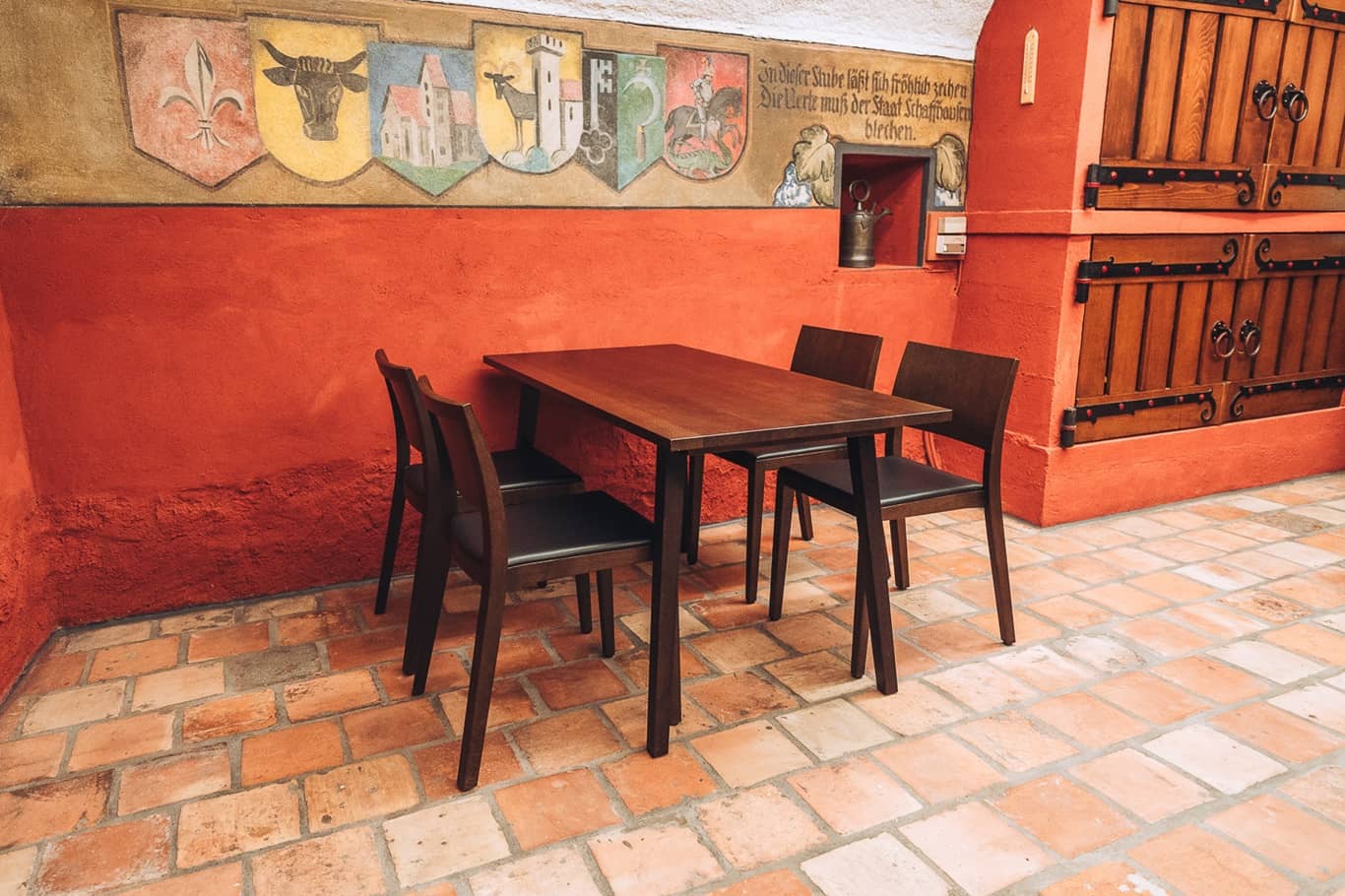 Im Staatskeller steht ein kleiner Tisch mit vier St&uuml;hlen neben den gezeichneten Kantonswappen an der Wand